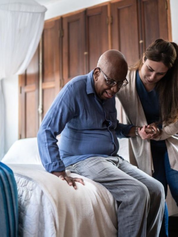 Home caregiver helping a senior man standing up at home