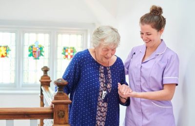 carer-helps-elderly-lady-in-blue-up-stairs-bannister_16x9